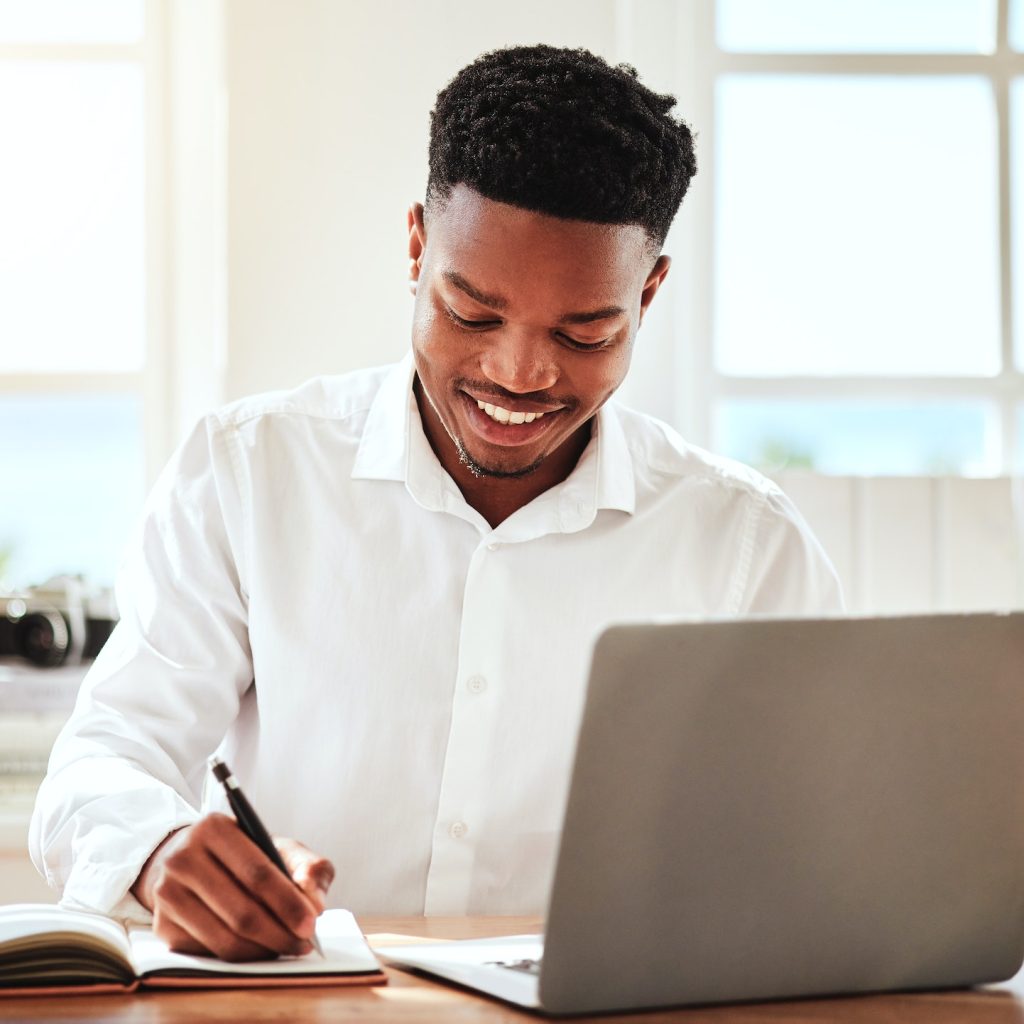 Internet, laptop and black man writing in notebook, happy freelance worker. African businessman wit